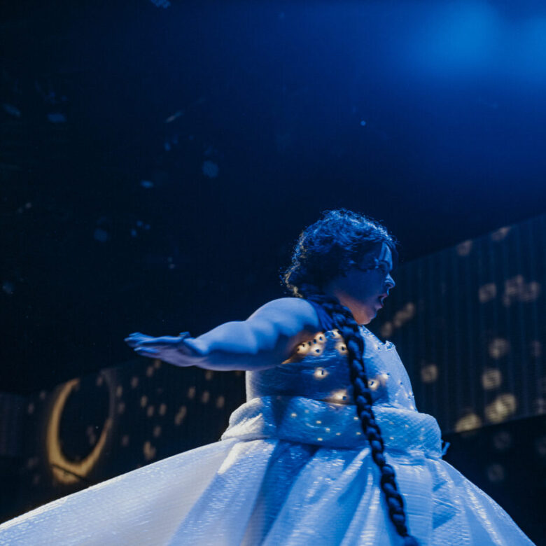 A person in a dress on stage under blue lights.