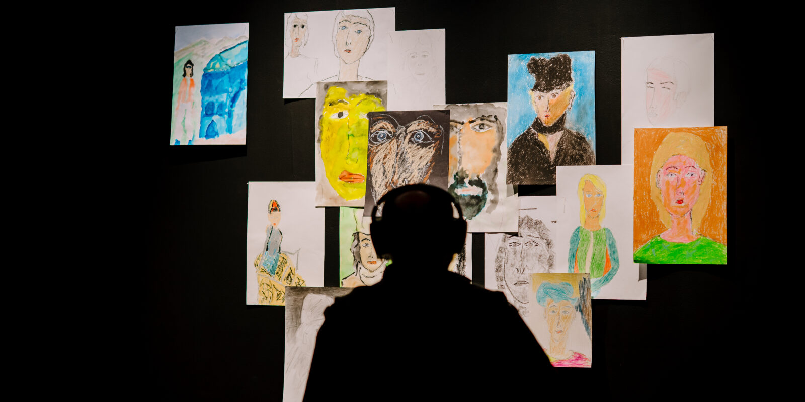 A shadow of a person looking at portraits on a wall.