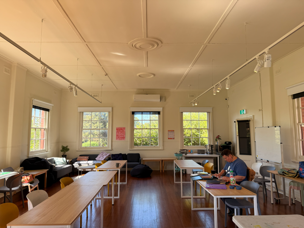 A light-filled room with desks, couches and bean bags. A person seated at a table working on their art.