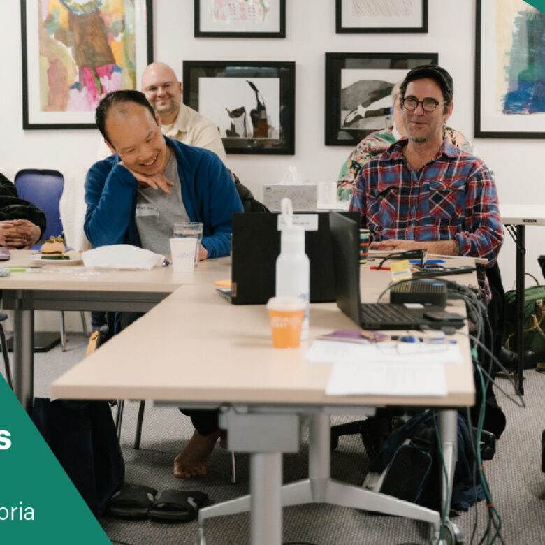 Creating Welcoming Environments. Workplace Training with Arts Access Victoria. 4 people seated at a desk in a room, smiling.