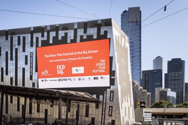 Outdoor screen at Fed Square showing an orange slide that reads ‘The Other Film Festival at the Big Screen’
