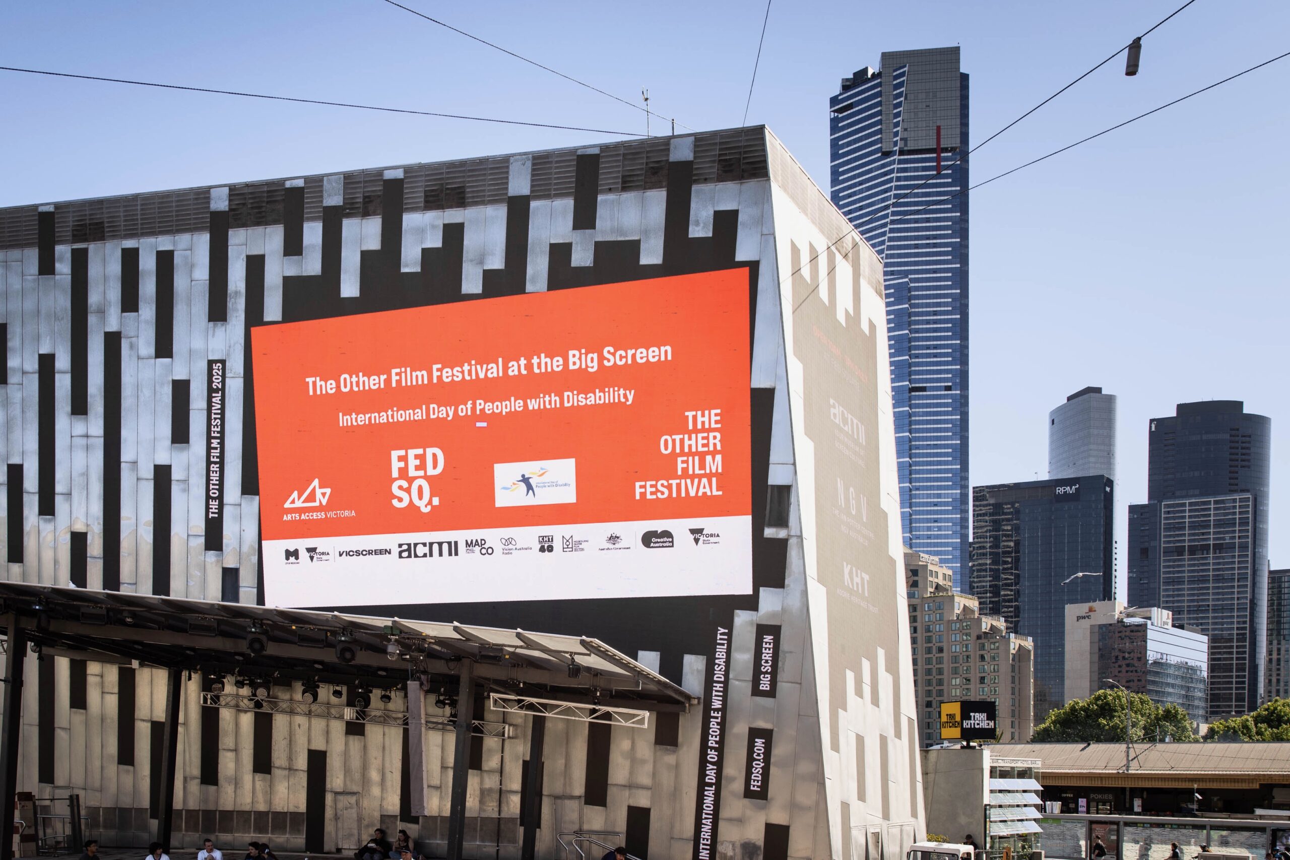 Outdoor screen at Fed Square showing an orange slide that reads ‘The Other Film Festival at the Big Screen’