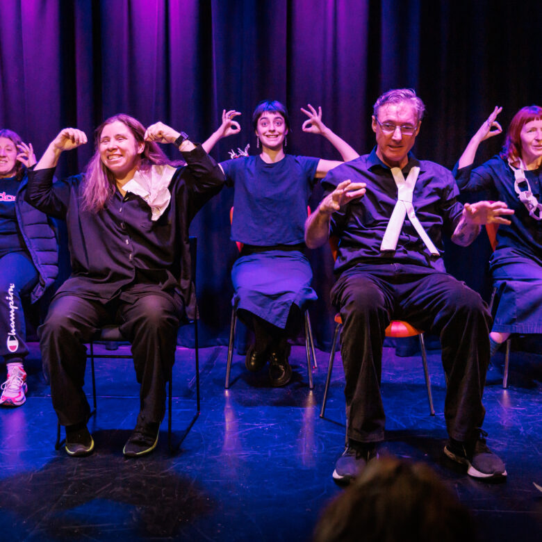 Five people seated on stage gesturing forward.