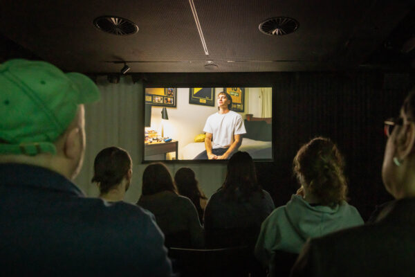People seated in a dark room and watching a film on screen.