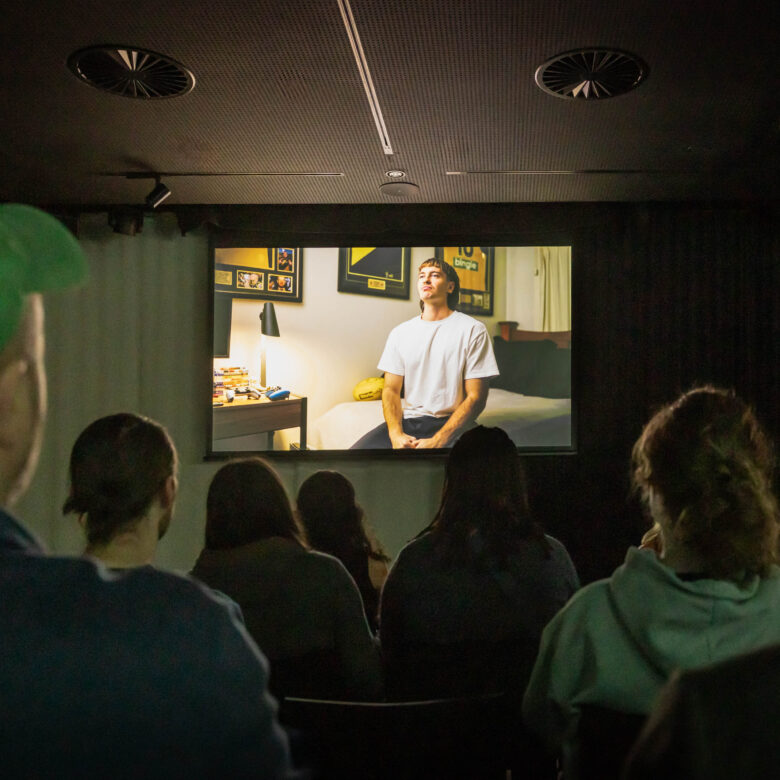People seated in a dark room and watching a film on screen.