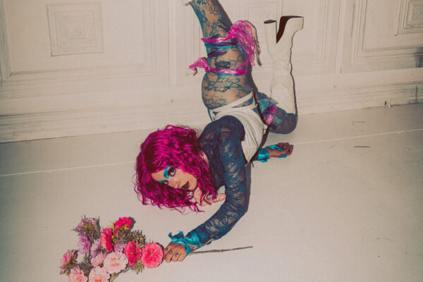 A performer doing a handstand against a wall looking at the camera.