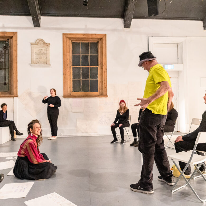 People standing and seated in an open hall rehearsing a performance.